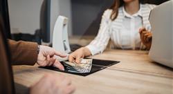 Businesswoman is working in exchange office. She is giving cash money to male customer.